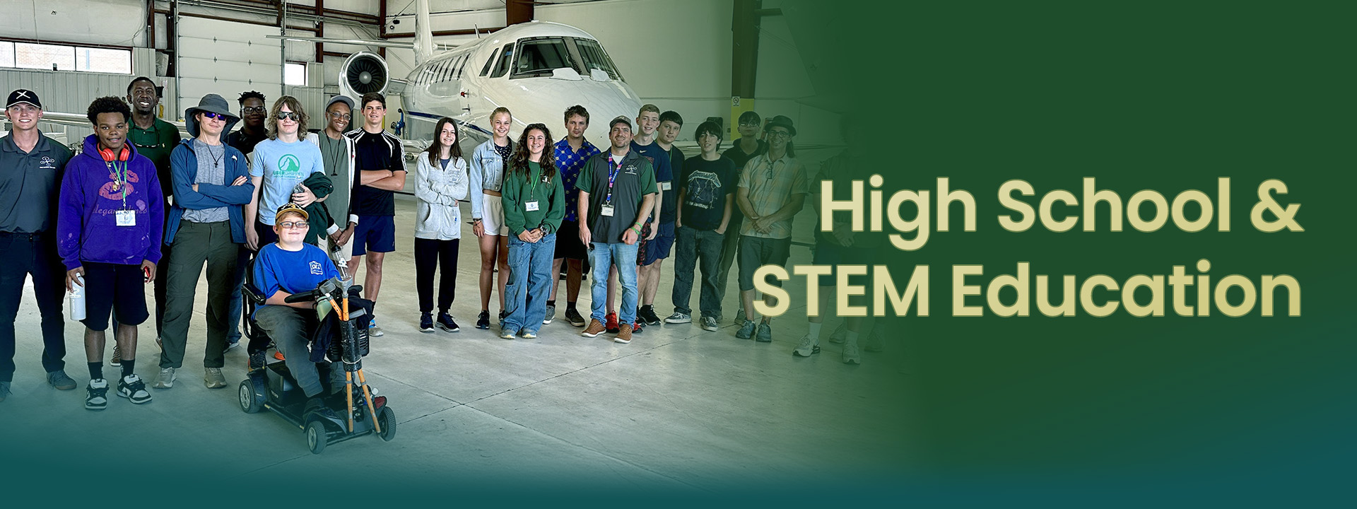 A diverse group of high school students engaged in STEM education inside an aviation facility.