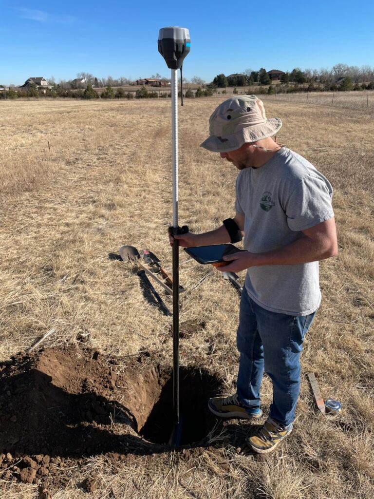 A person measures soil depth with a probe in a field on a sunny day.